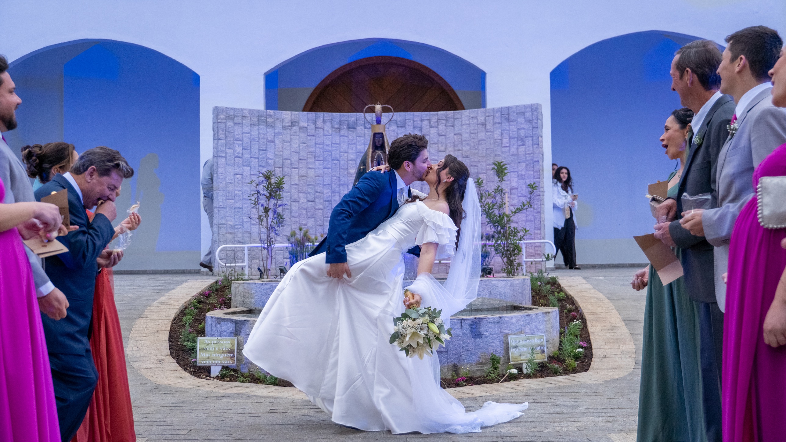 Noivos se beijando na saída da igreja, entre os convidados