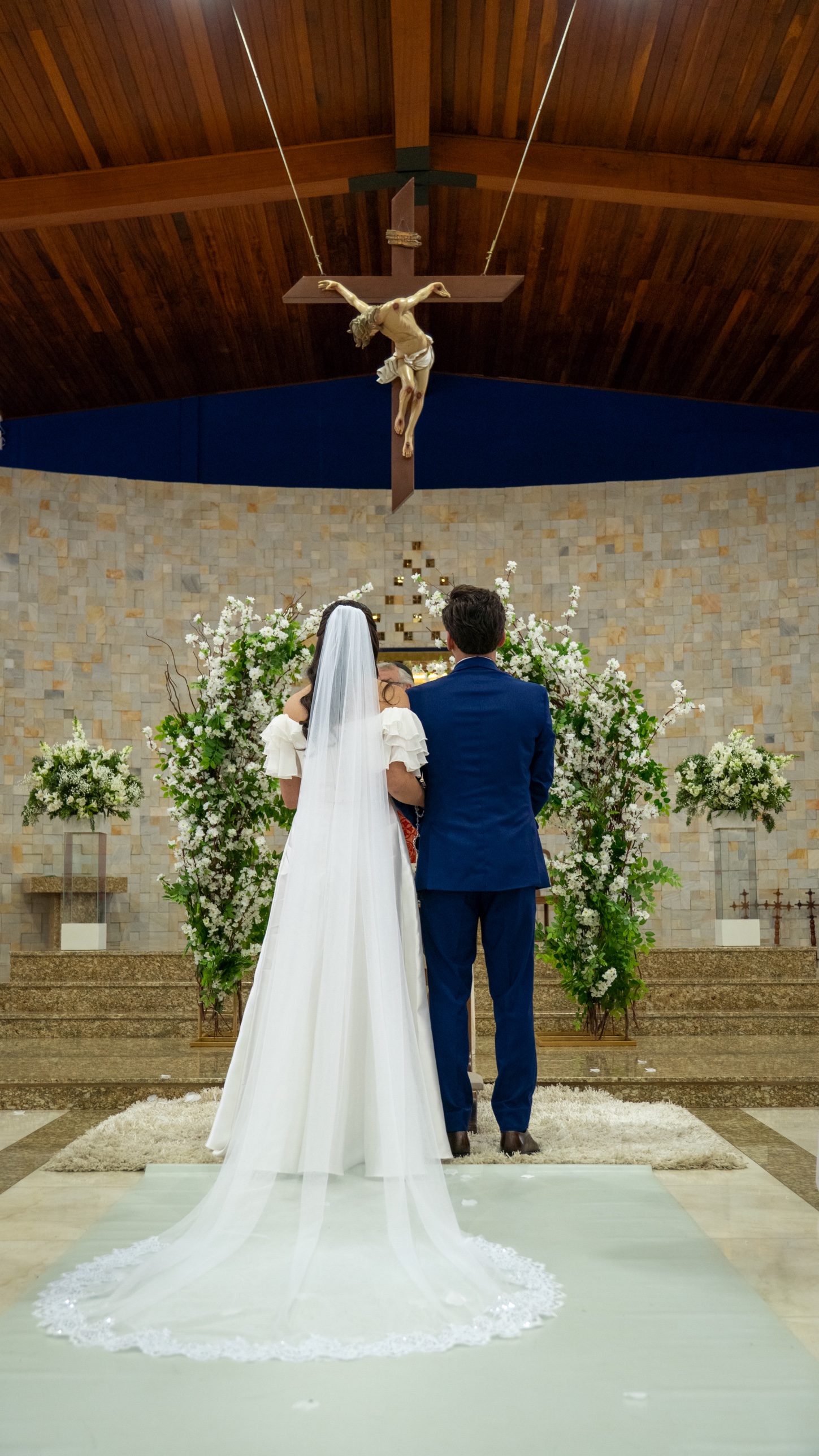 Noivos de costas no altar, com o véu estendido sobre o tapete