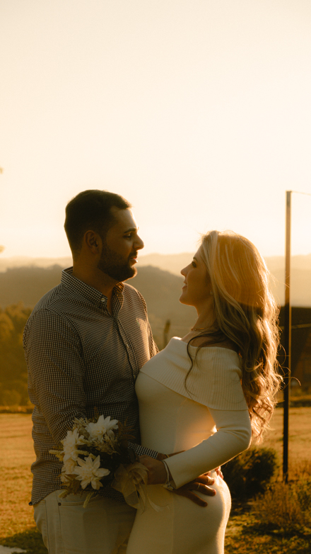 Casal se olhando ao entardecer, ela segurando um buquê