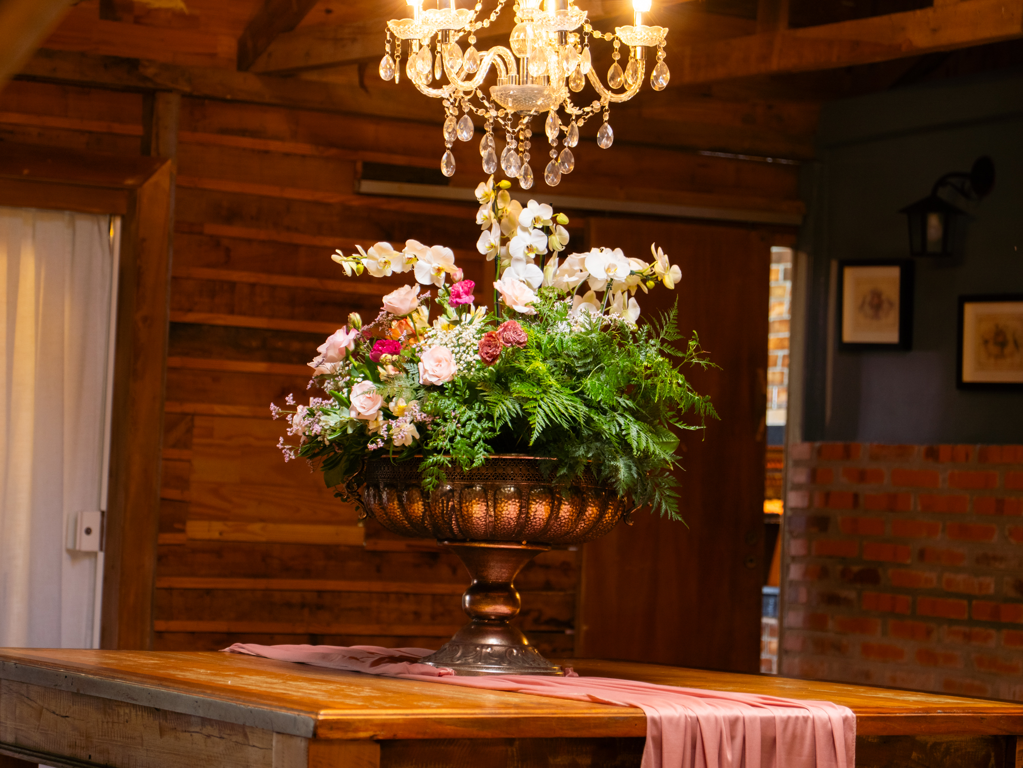 Arranjo de orquídeas e rosas em vaso de cobre sob o lustre de cristal