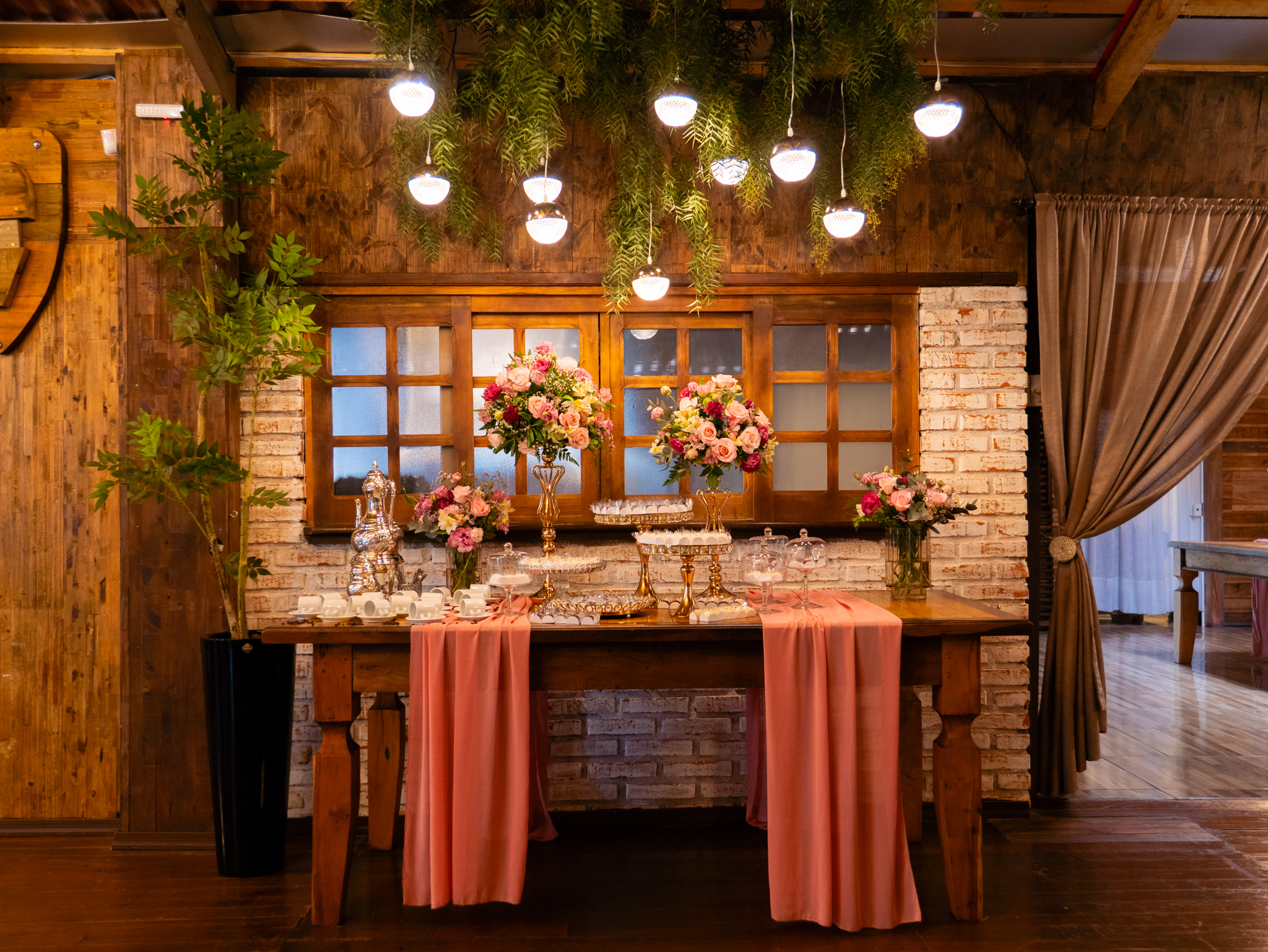 Mesa de doces com flores e luminárias pendentes, em salão de madeira