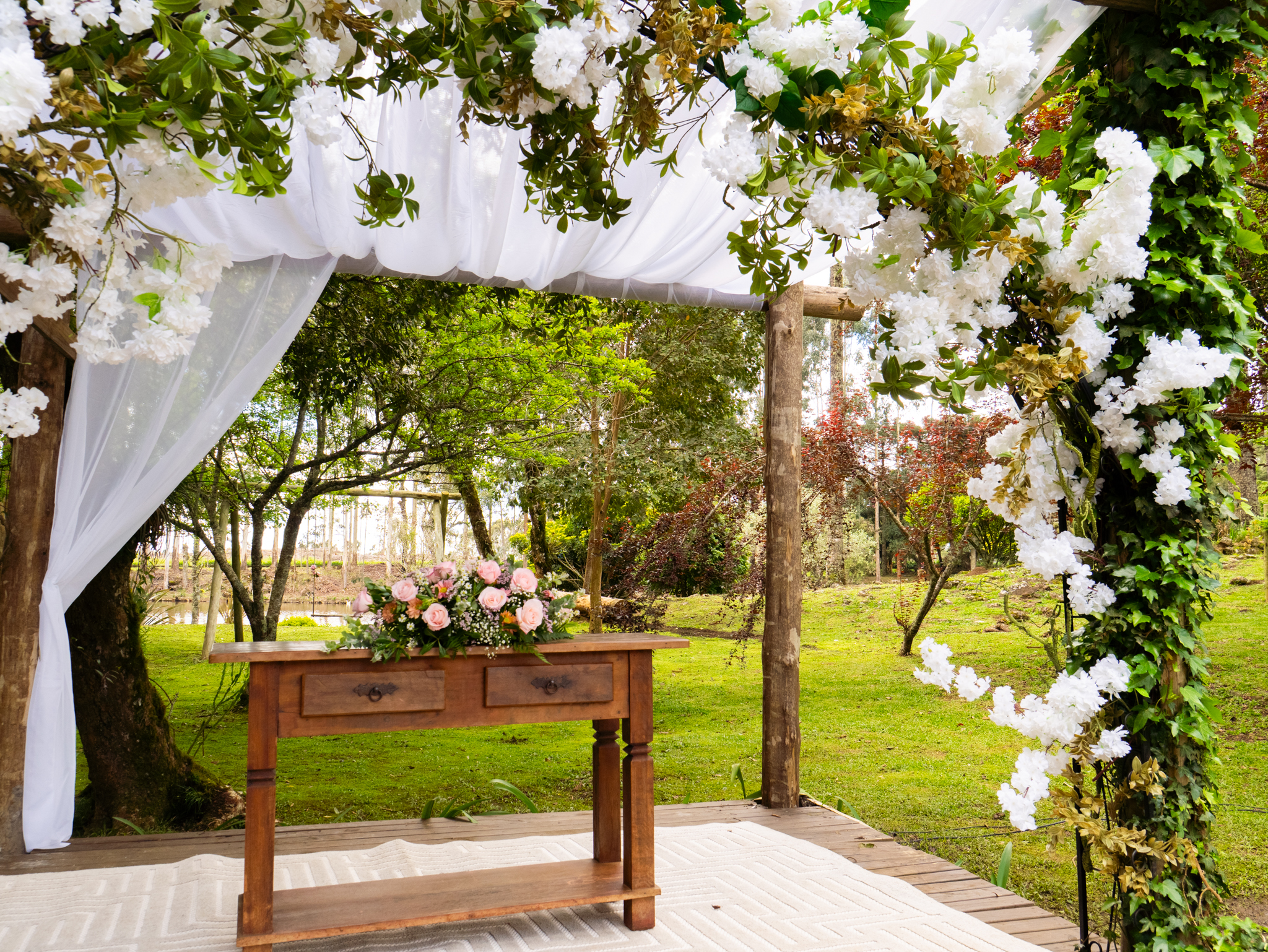 Altar sob pergolado com flores brancas e tecido