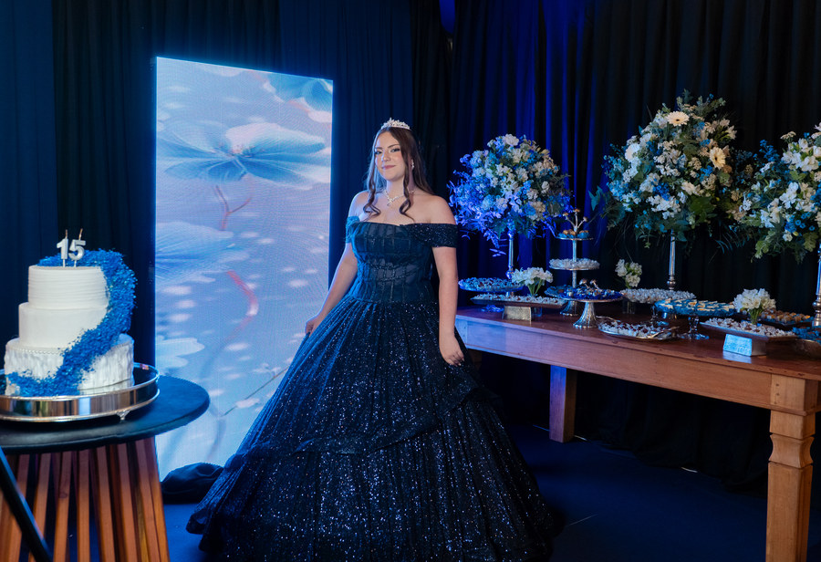 Debutante ao lado do bolo e da mesa de doces decorada em azul
