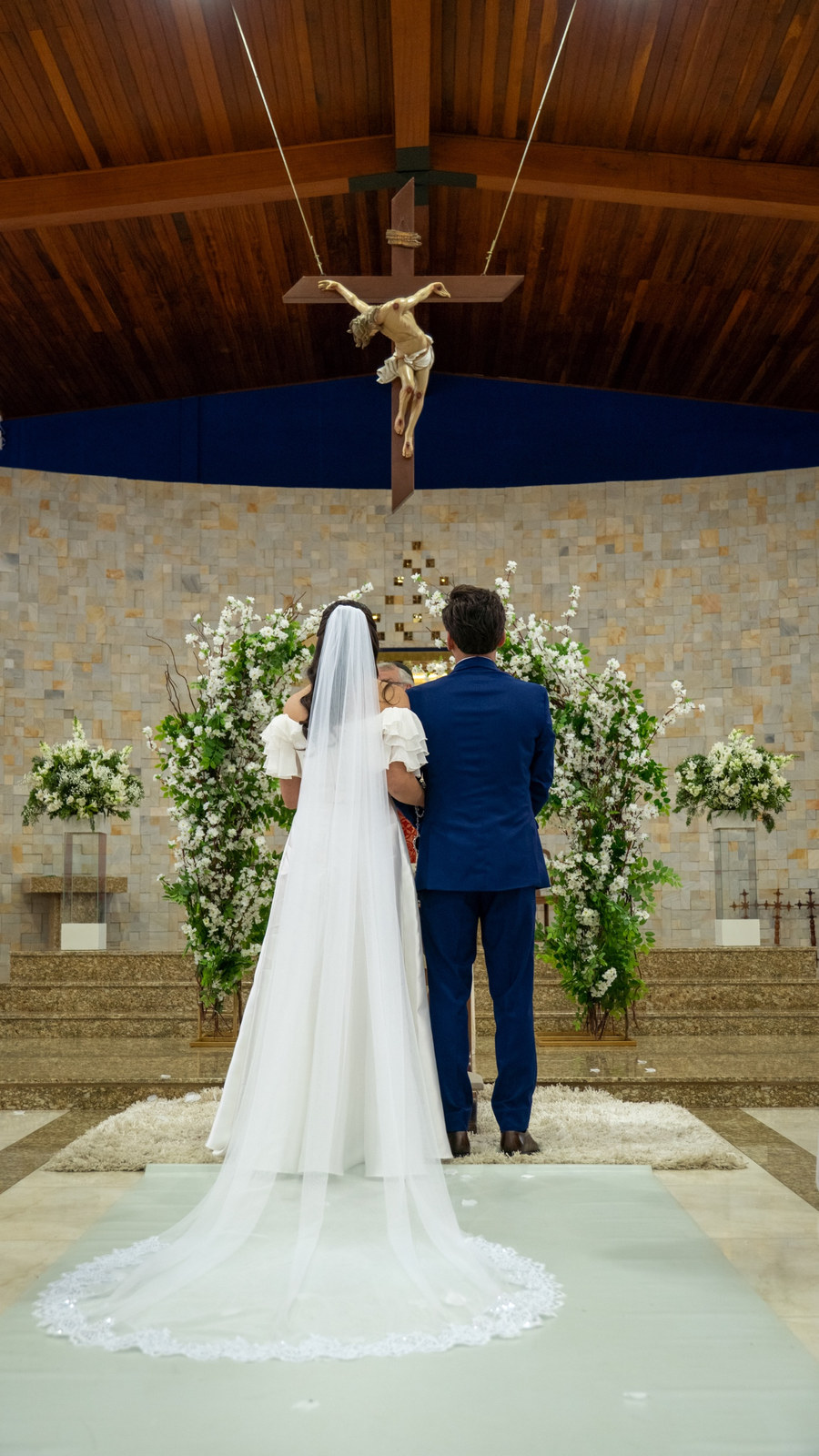 Noivos de costas no altar, com o véu estendido sobre o tapete