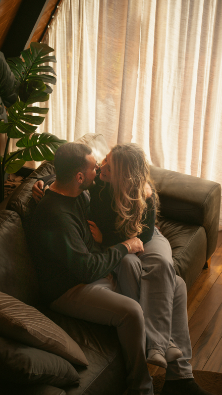 Casal abraçado em um sofá, perto da janela