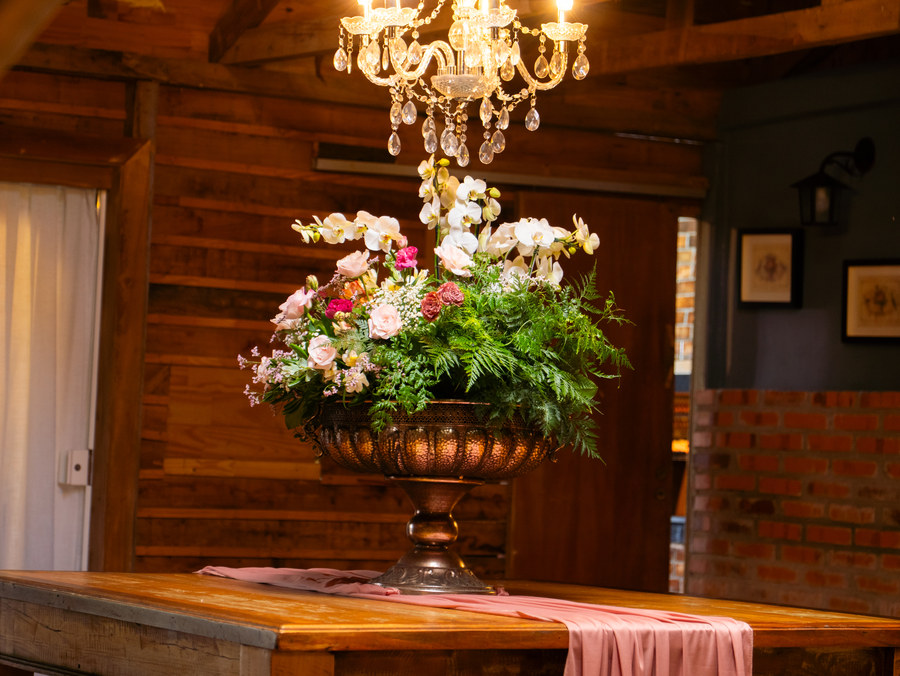 Arranjo de orquídeas e rosas em vaso de cobre sob o lustre de cristal