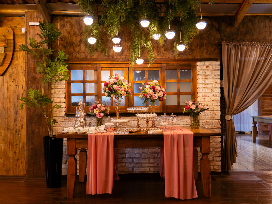 Mesa de doces com flores e luminárias pendentes, em salão de madeira